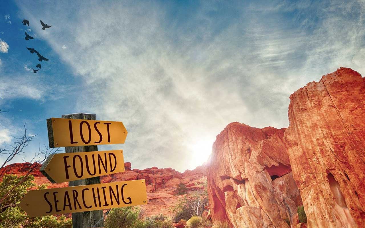 A signpost set against a desert sky reads lost, found, searching.