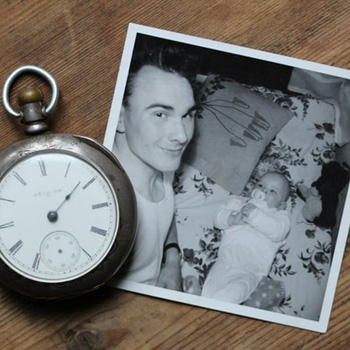 A black and white photo of a man and a baby, with a pocket-watch sitting beside the photo.