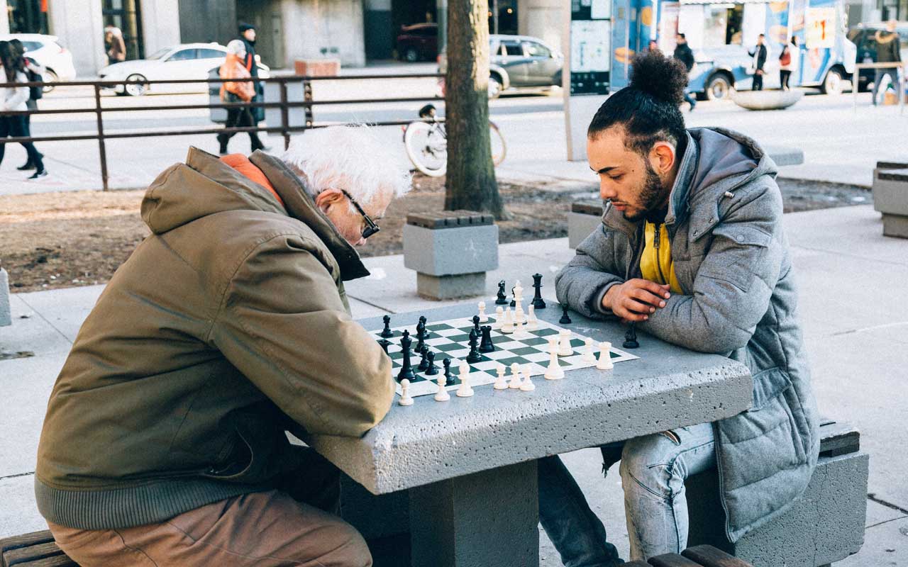 Un uomo anziano gioca a scacchi nel parco con un uomo più giovane. Gli scacchi sono un tipo di attività cognitive per adulti che possono essere utili con l'età.