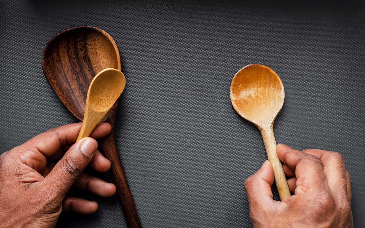 Een persoon houdt houten lepels in zijn handen, met een tussenruimte op een tafel.