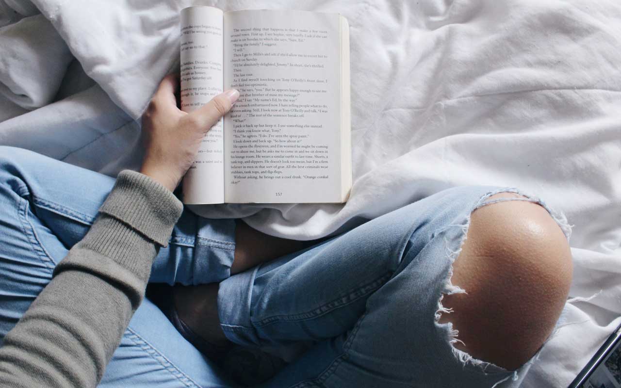 A person sits on a bed holding a book, while using a Visualizing reading strategy.