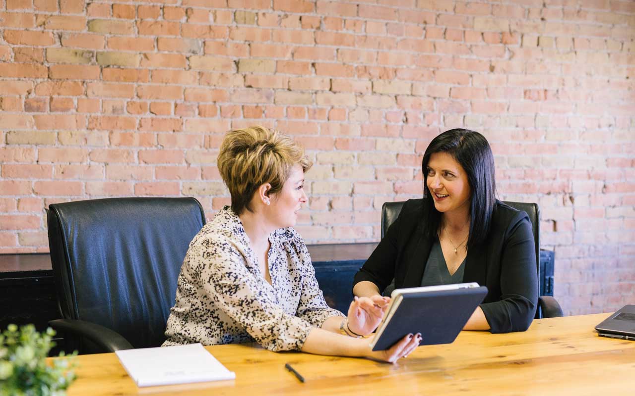 Two women sit at a desk. Hiring a coach to keep yourself accountable can help you stay focused while studying.