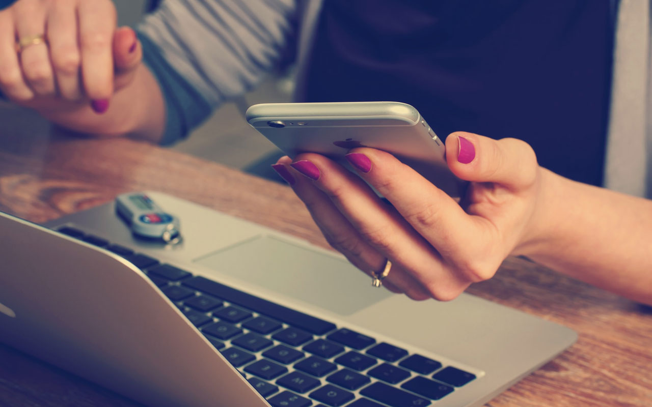A woman holds her phone while working on her laptop. Too many devices can hurt your ability to concentrate on studies.
