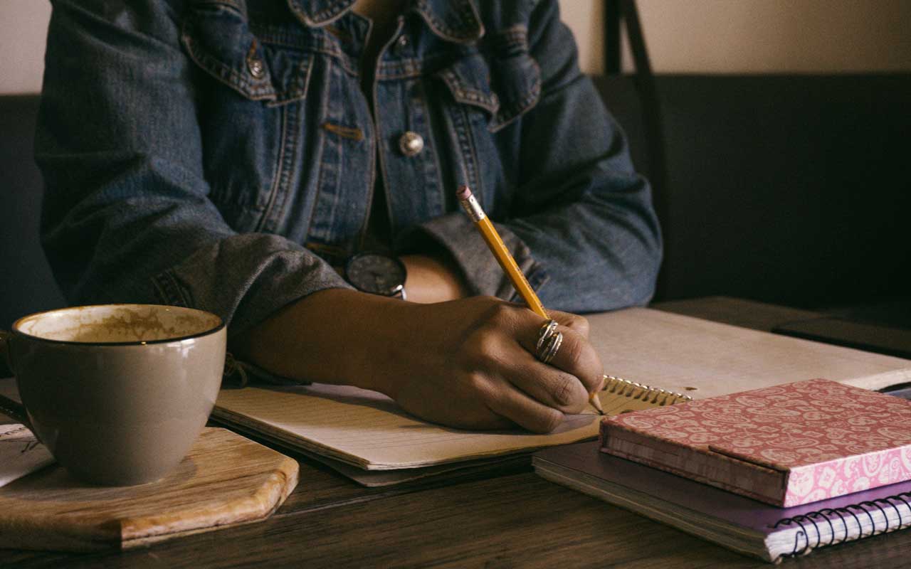A person writes in a notebook. Writing summaries of what you just read is an important visualization reading strategy.