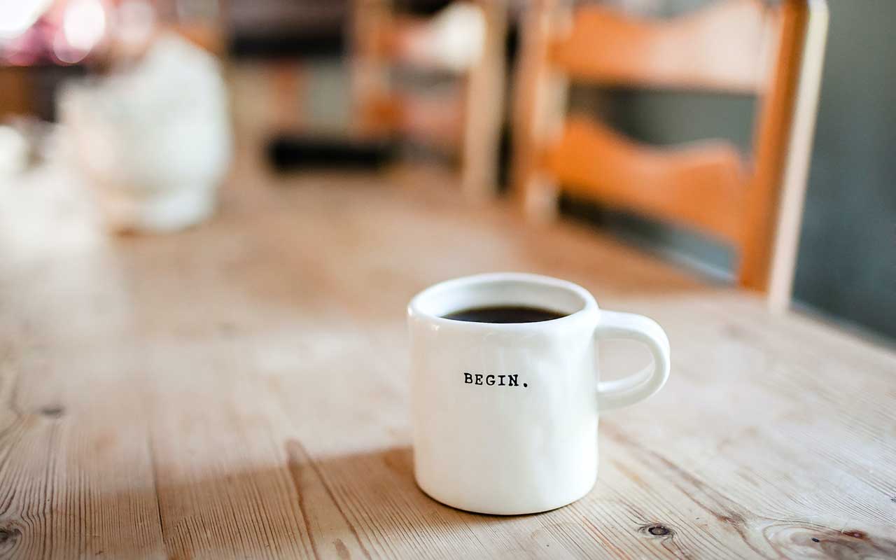 A white mug with the word "begin" sits on a wooden table.