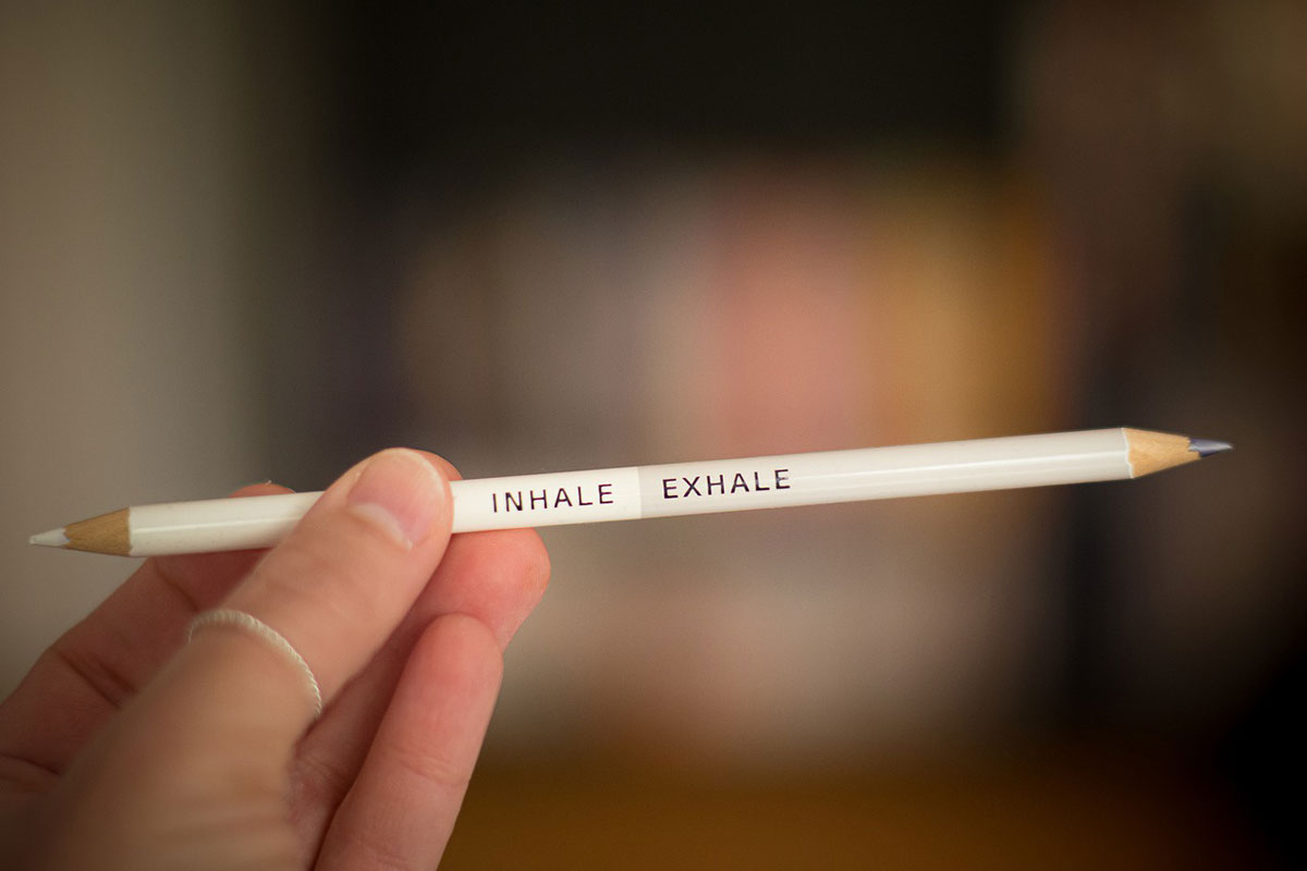 A person holds a double-sided pencil with the words "inhale" and "exhale" printed on it.