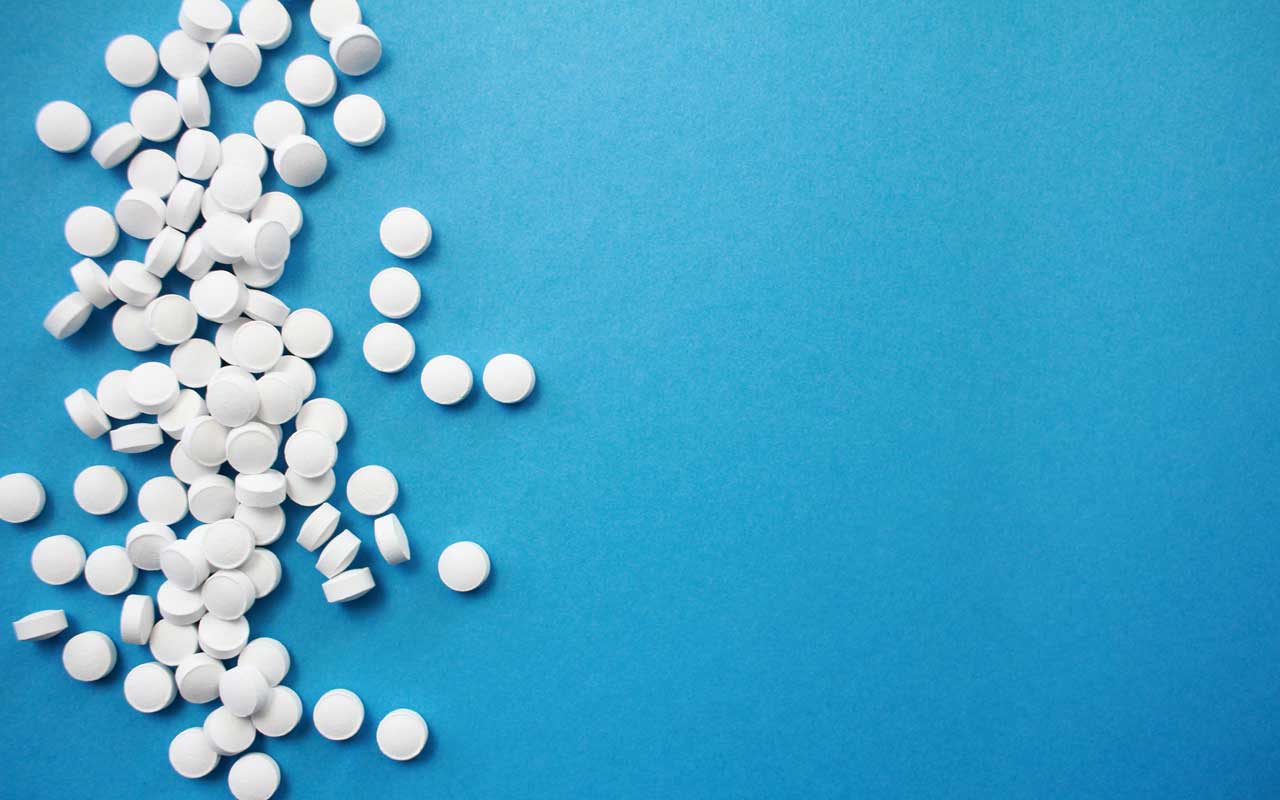 White pills spill across a blue surface. Substance abuse often lead to memory impairment.