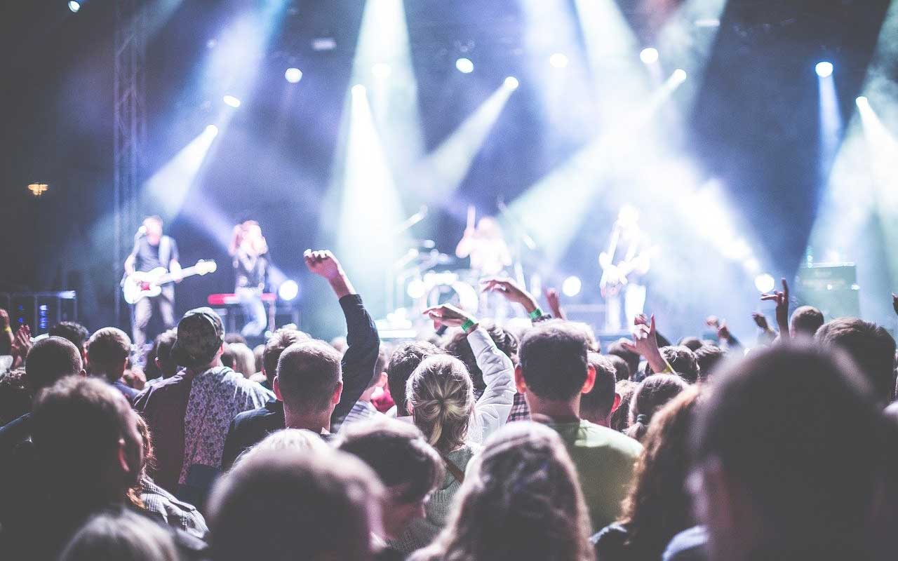 A rock band plays on stage. The view of the stage and lights is from in the audience.