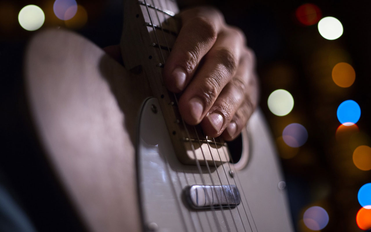 A person's hand sits on the frets of a guitar.