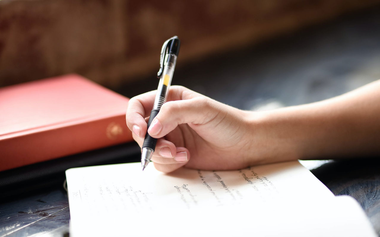 A person writes in a notebook with a ballpoint pen. Writing is one of the "big five" language skills.