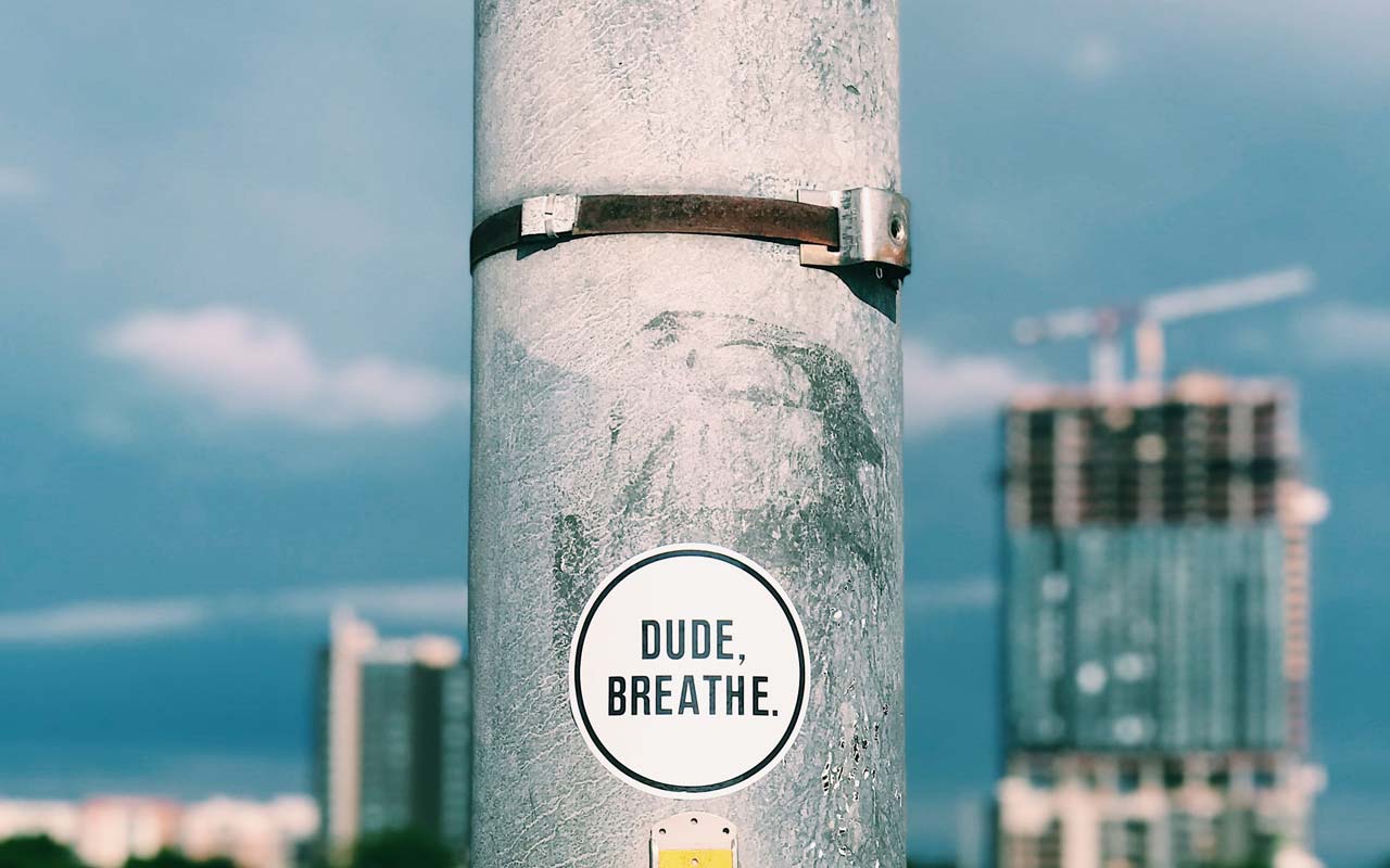 A sticker on a pole (overlooking a cityscape) reads "Dude, breathe."