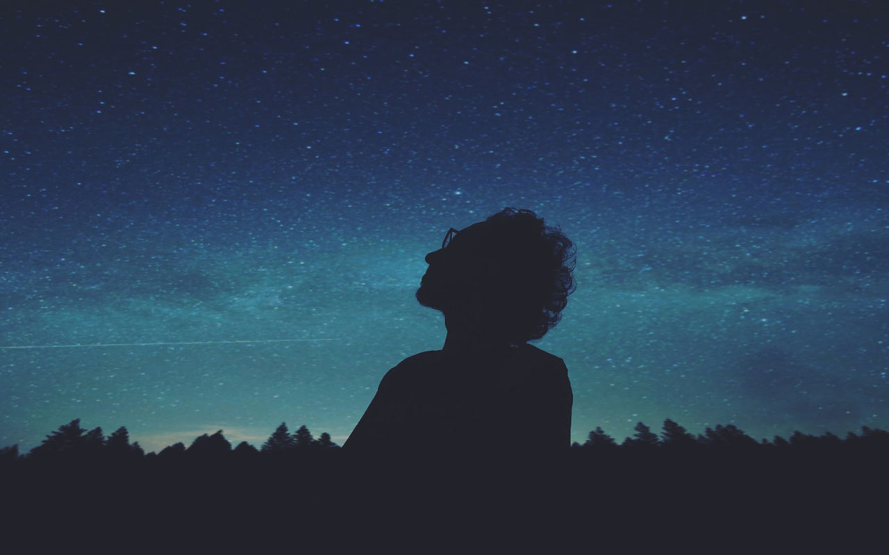 A person stares up at the night sky full of stars. Better focus can be a result of this concentration meditation.