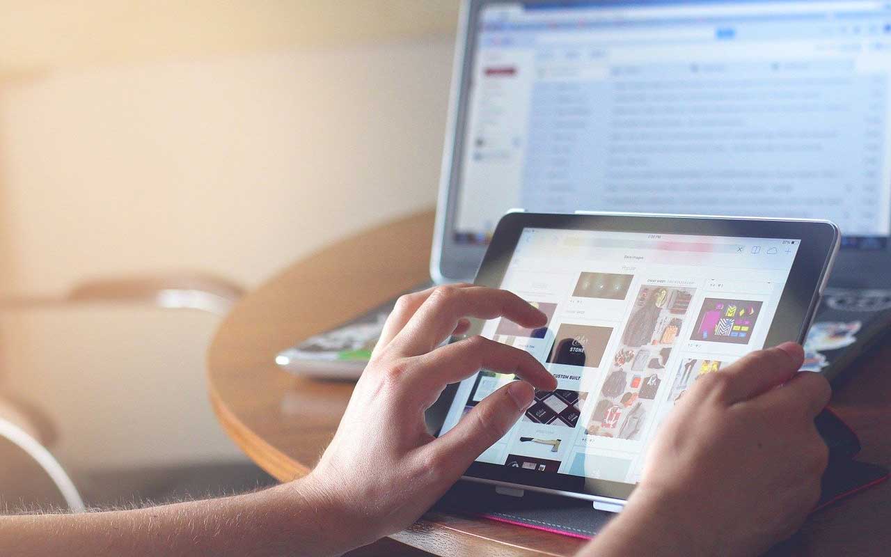 A person scrolls through Pinterest on their tablet while their laptop rests behind the tablet screen.