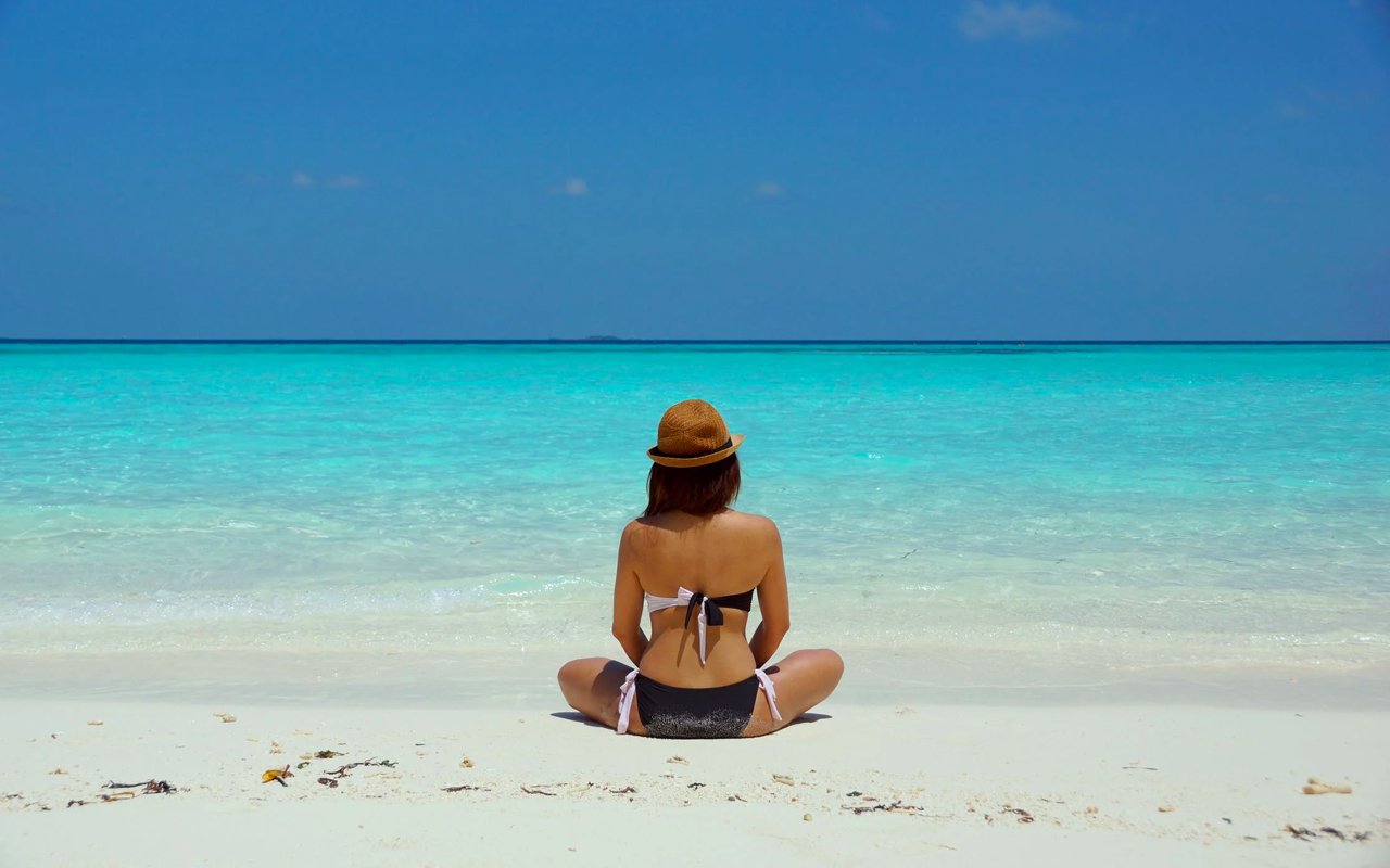 woman wearing a brown hat is meditating on a beach